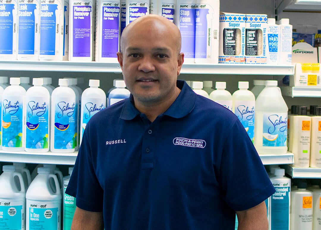 3. Pinch A Penny employee owner in front of pool chemicals shelf.