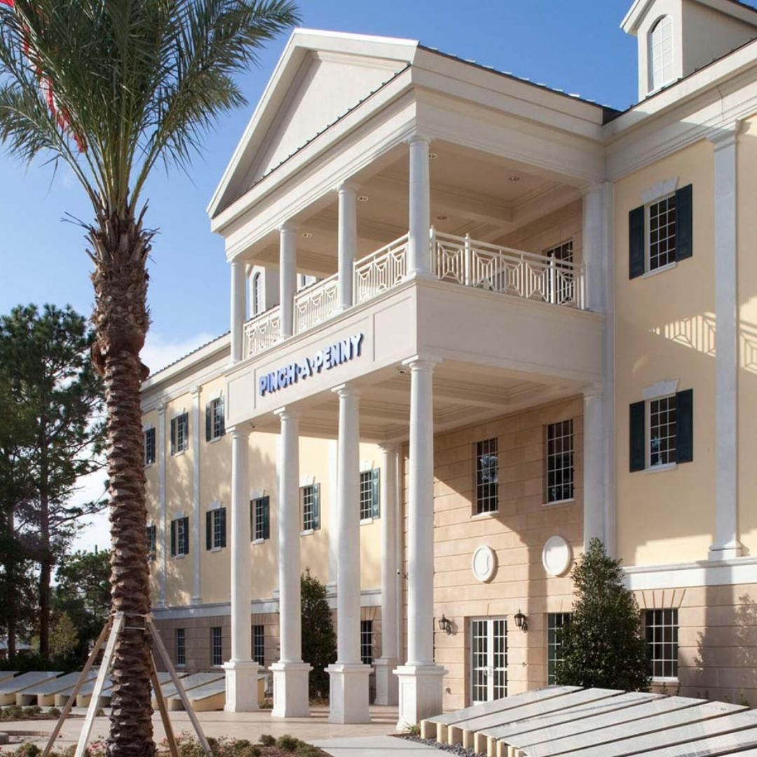 Exterior of a large Pinch A Penny building with white columns and a balcony, with the Pinch A Penny sign centered on the facade.