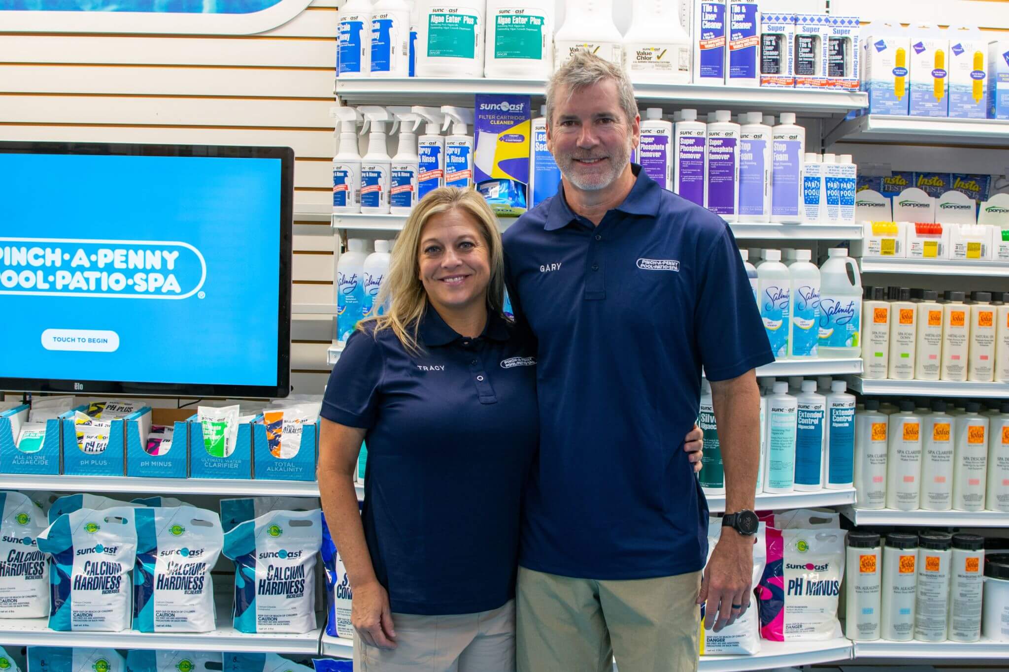 Pinch A Penny owners smiling in uniform while posing in front of a retail display