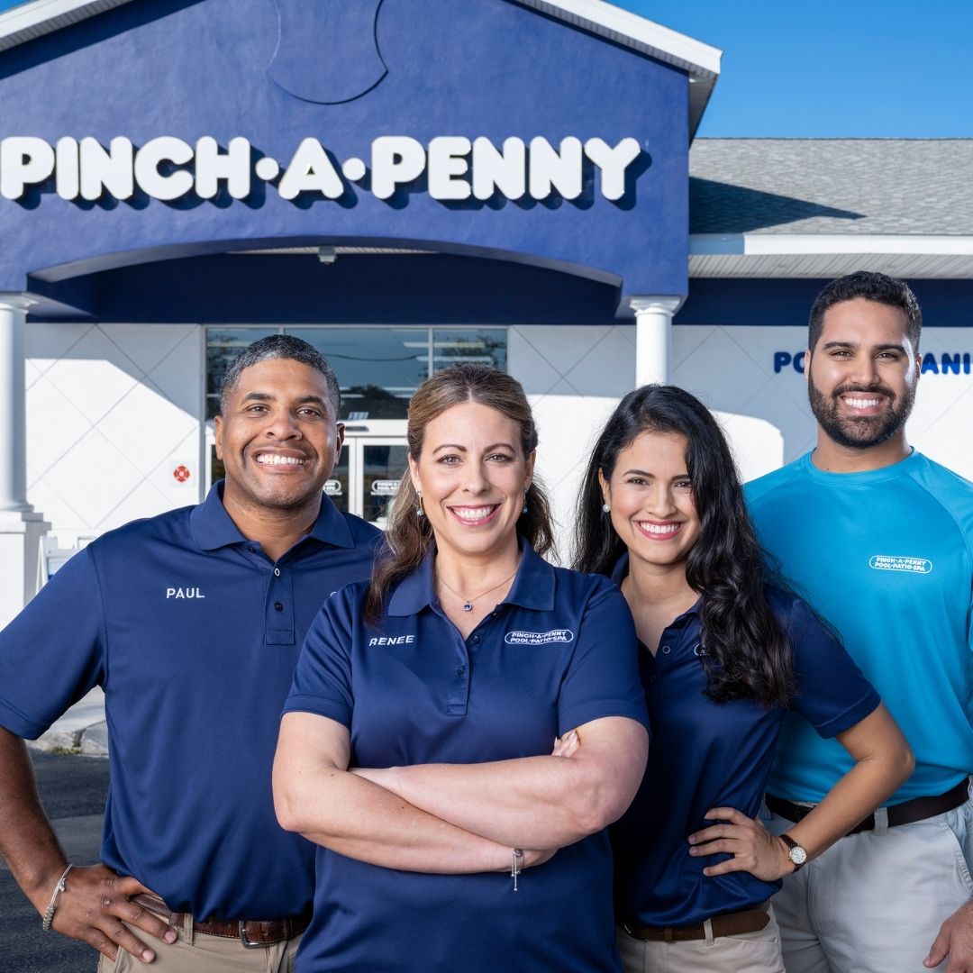 Group of Pinch A Penny team members standing in front of a store, smiling toward the camera in branded uniforms.