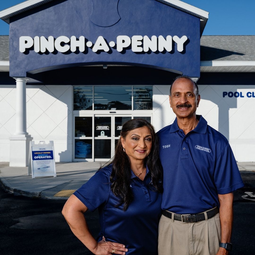 Two Pinch A Penny store owners standing confidently in front of their storefront.