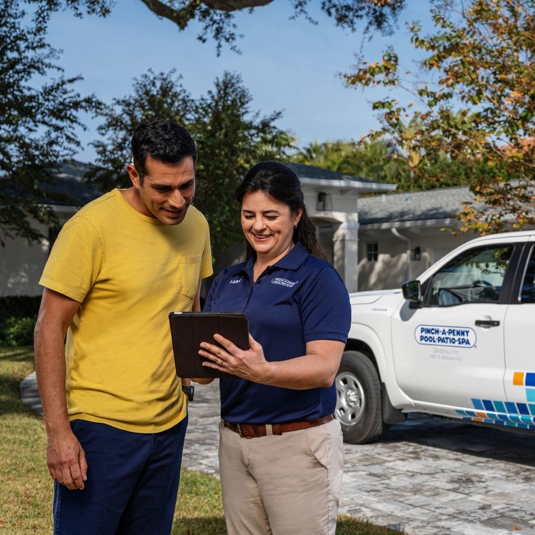 Pinch A Penny team member reviewing tablet with homeowner in driveway beside branded service truck