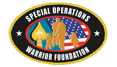 The Special Operations Warrior Foundation logo, featuring gold silhouettes of military figures and children in front of an American flag. A gold torch symbol appears on the left, surrounded by a black oval border with white stars and the words “Special Operations Warrior Foundation.”