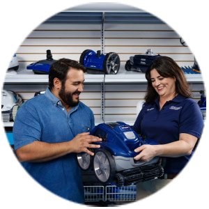 Two employees in a pool supply store reviewing an automatic pool cleaner with additional pool equipment displayed on shelves behind them.