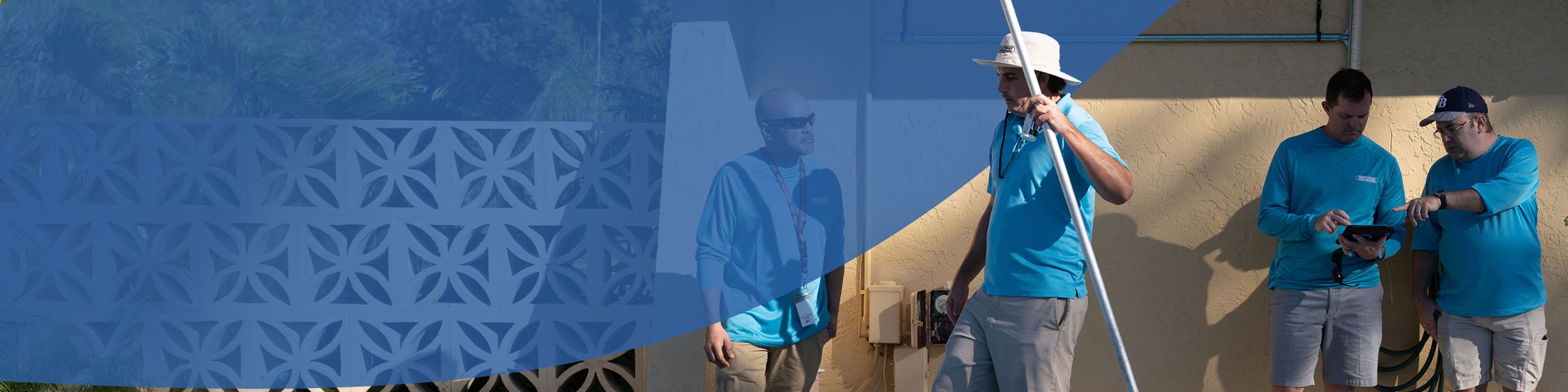 Four pool technicians in blue shirts, one holding long pole while two review tablet