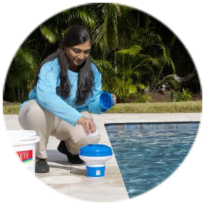 Woman testing and treating residential pool water at the poolside using cleaning supplies and pool chemicals.